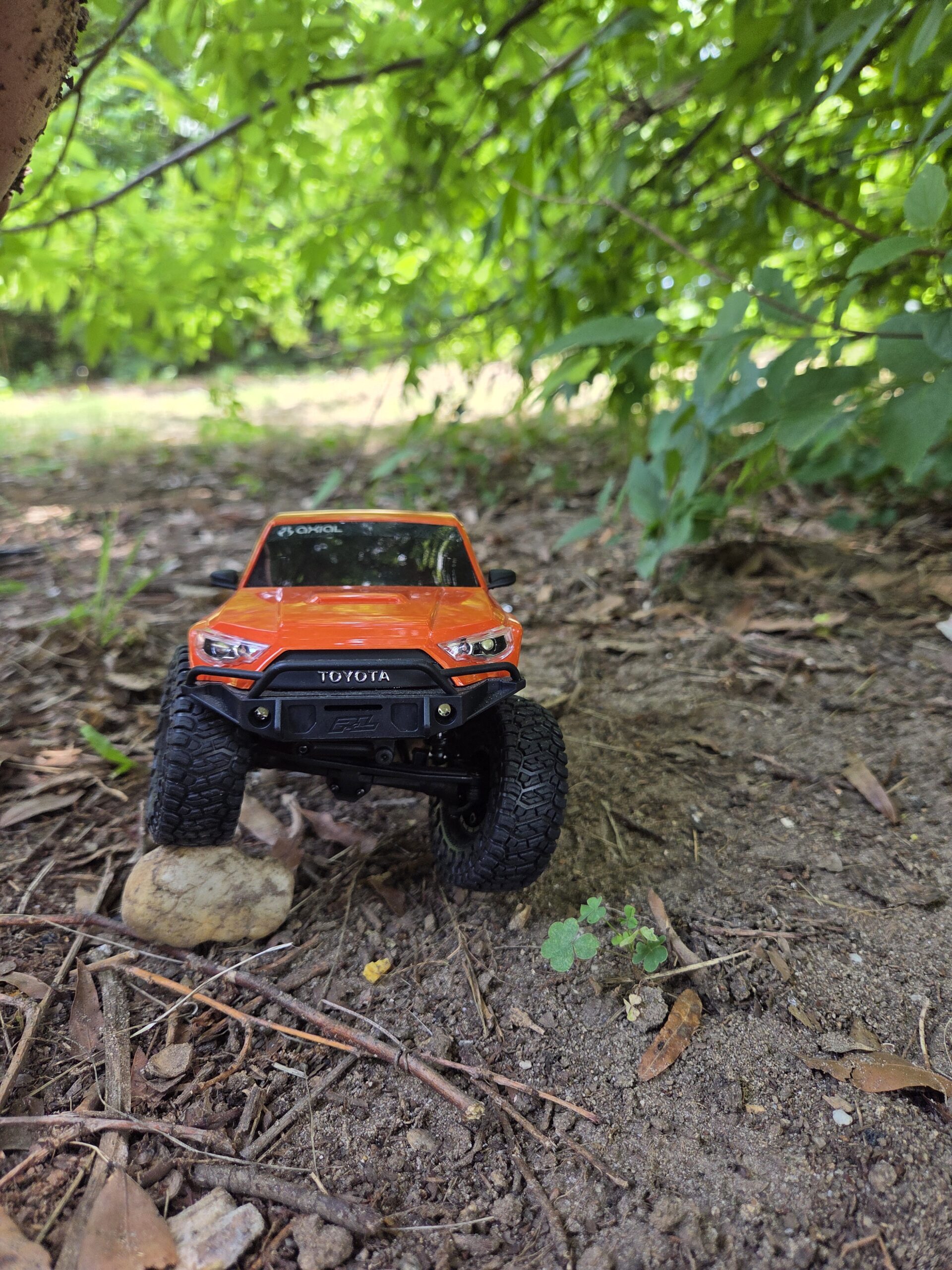 Axial SCX24 Toyota 4Runner orange attacking a log obstacle from the front in wooded setting