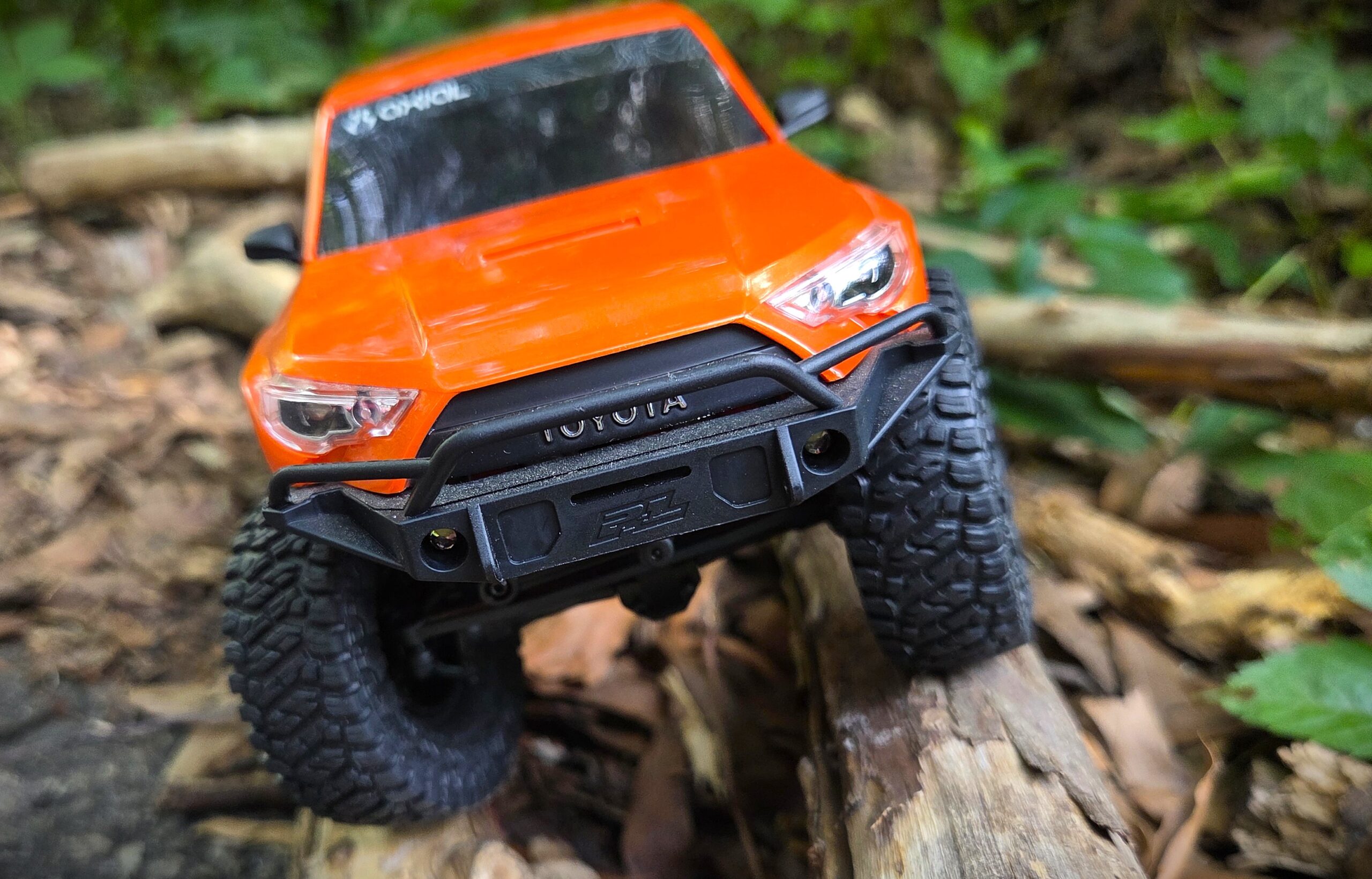 Close front-facing shot of orange Axial SCX24 Toyota 4Runner on a log, Toyota badge and bumper lights visible