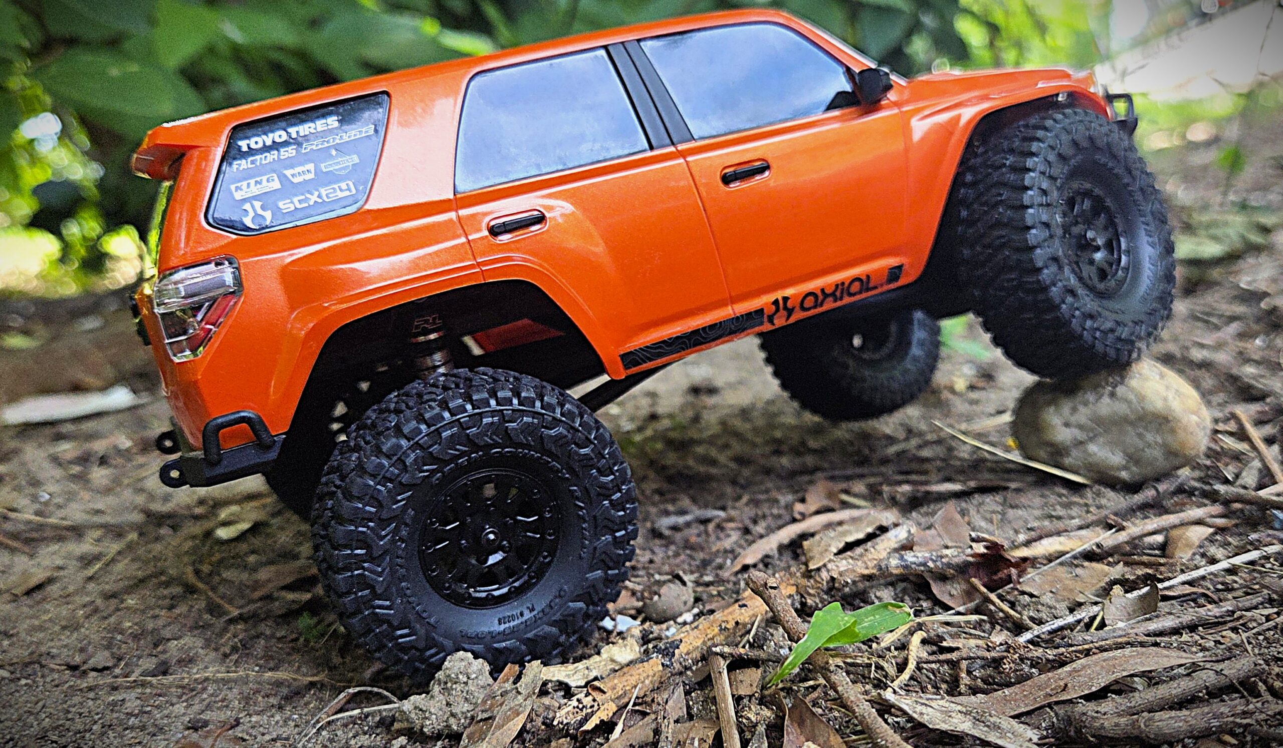 Axial SCX24 Toyota 4Runner orange, rear three-quarter view while climbing terrain in natural setting